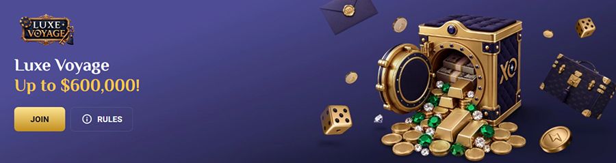 RollXO Casino promotional hero banner for the Luxe Voyage campaign set on a dark purple background. Left side features the gold LUXE VOYAGE logo above white and gold headline text reading "Luxe Voyage Up to $600,000!" with a gold "JOIN" button and "RULES" info icon. Right side showcases an open luxury gold-trimmed bank vault with XO branding spilling gold bullion bars, emeralds, diamonds, and gold coins, surrounded by floating golden dice, a designer travel trunk, gold coins, and a sealed wax envelope.